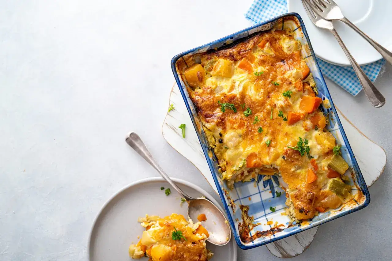 Un gratin de courge aux légumes, doré et appétissant, servi dans un plat bleu et blanc. Une portion est déjà servie dans une assiette.