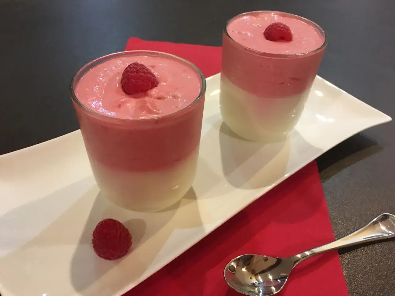 Deux verrines de mousse chocolat blanc et framboise, garnies d'une framboise fraîche.