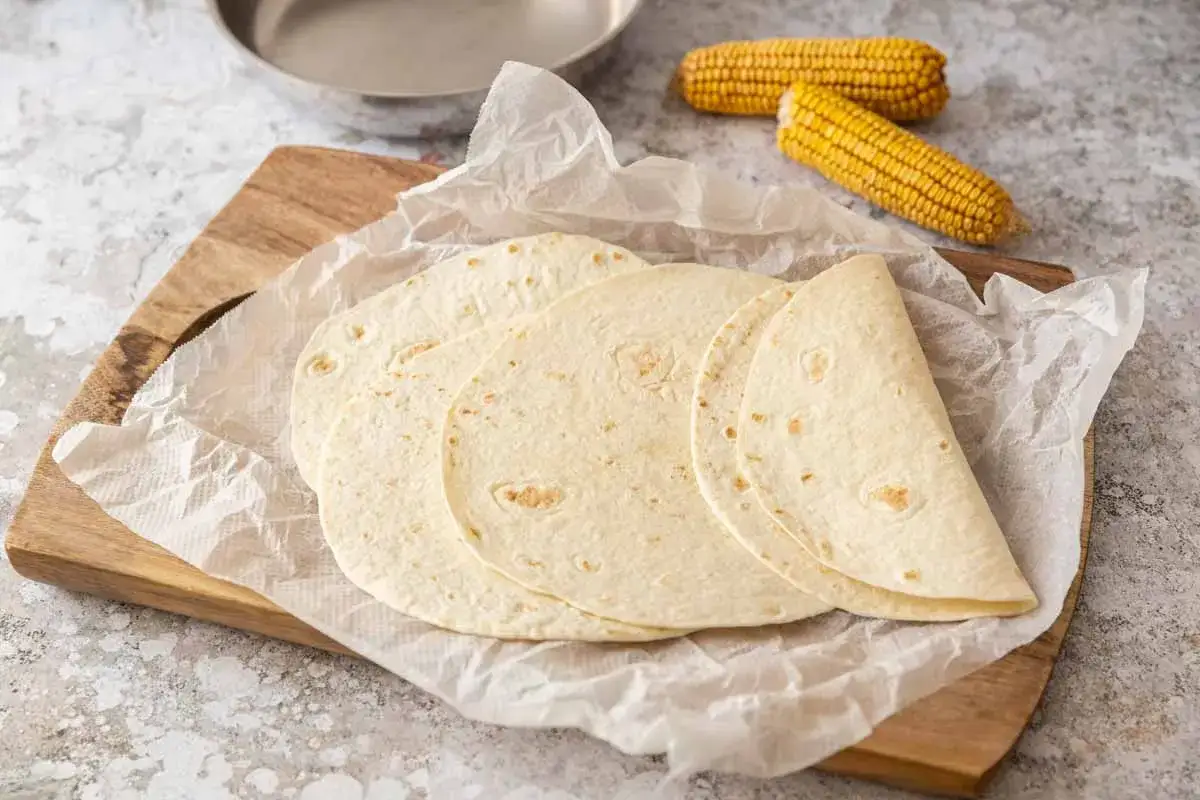 Des tortillas maison prêtes à être garnies, avec des épis de maïs en arrière-plan. Parfait pour une recette facile et savoureuse.