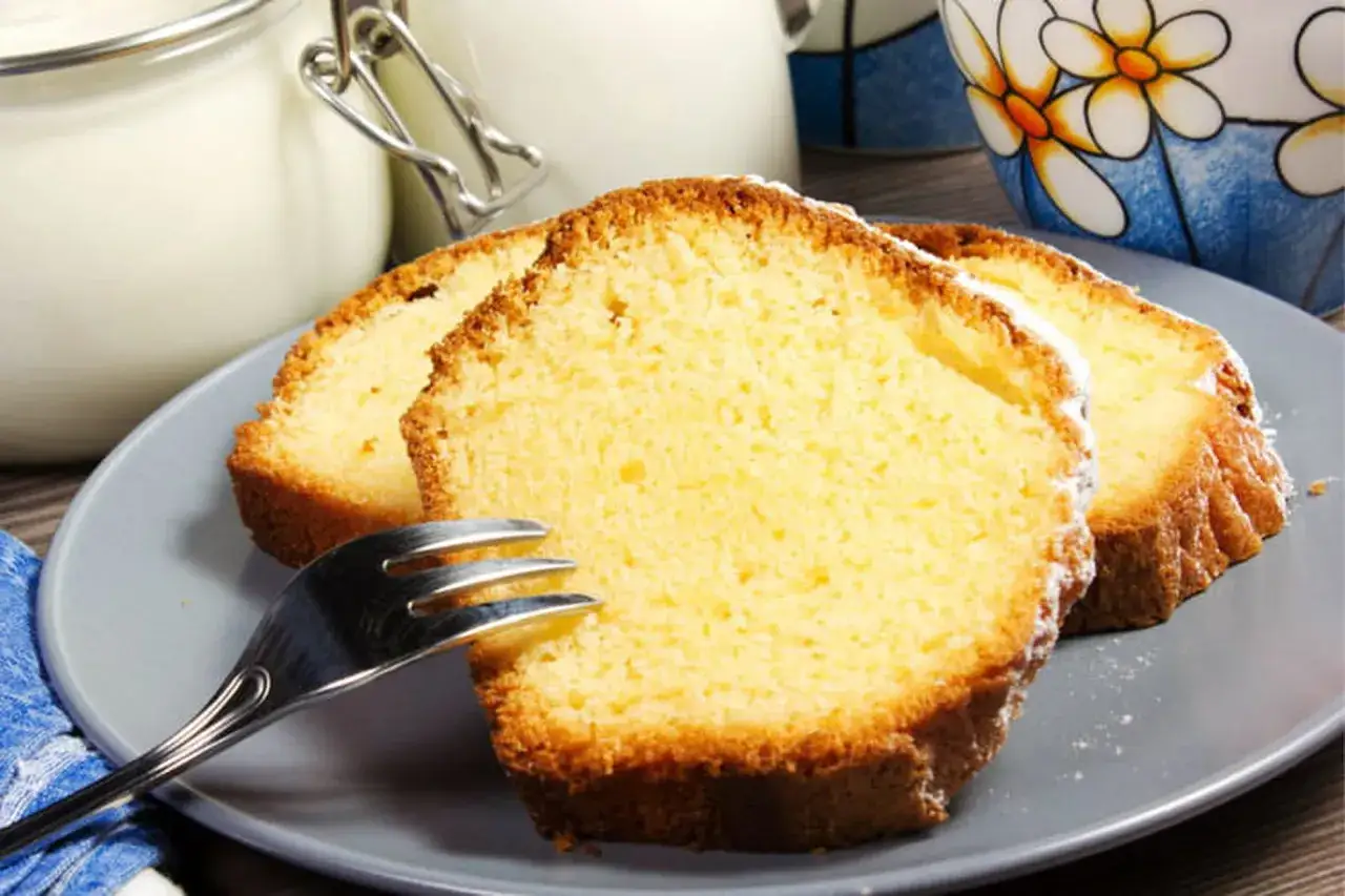 Tranches de g&acirc;teau moelleux sur une assiette grise, parfaites pour une recette g&acirc;teau facile et rapide. Une tasse d&eacute;cor&eacute;e et un pot en verre sont en arri&egrave;re-plan.