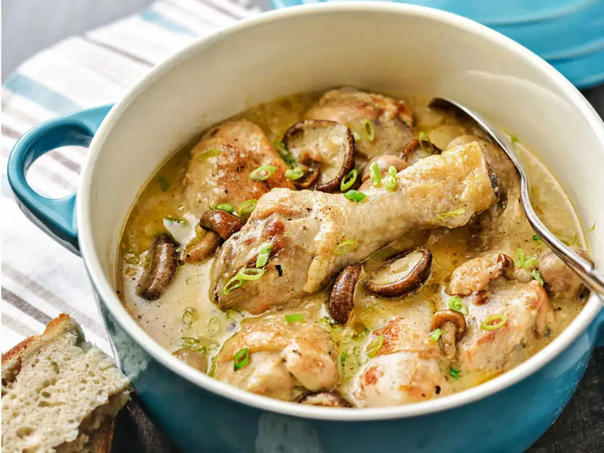 Un savoureux poulet aux champignons mijot&eacute; dans une sauce cr&eacute;meuse, garni de ciboule fra&icirc;che. Une cuill&egrave;re et du pain rustique sont pr&ecirc;ts &agrave; &ecirc;tre d&eacute;gust&eacute;s.