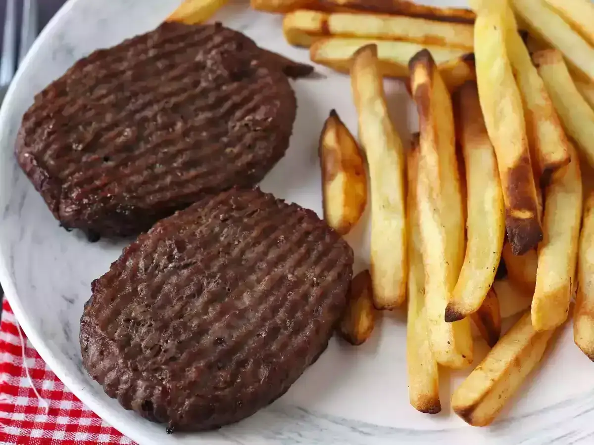 Deux steaks hach&eacute;s parfaitement grill&eacute;s, accompagn&eacute;s de frites dor&eacute;es, un d&eacute;lice pr&eacute;par&eacute; &agrave; l'air fryer.