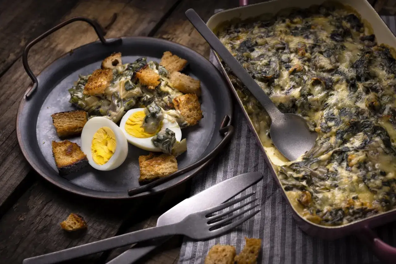 Un plat de gratin de blettes, garni de croûtons et d'un œuf dur, prêt à être dégusté.