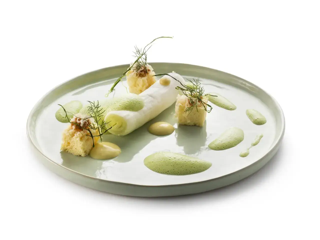 Poireaux à la crème, présentés avec des cubes de pain brioché, des éclats de noix et une émulsion verte sur une assiette pastel.