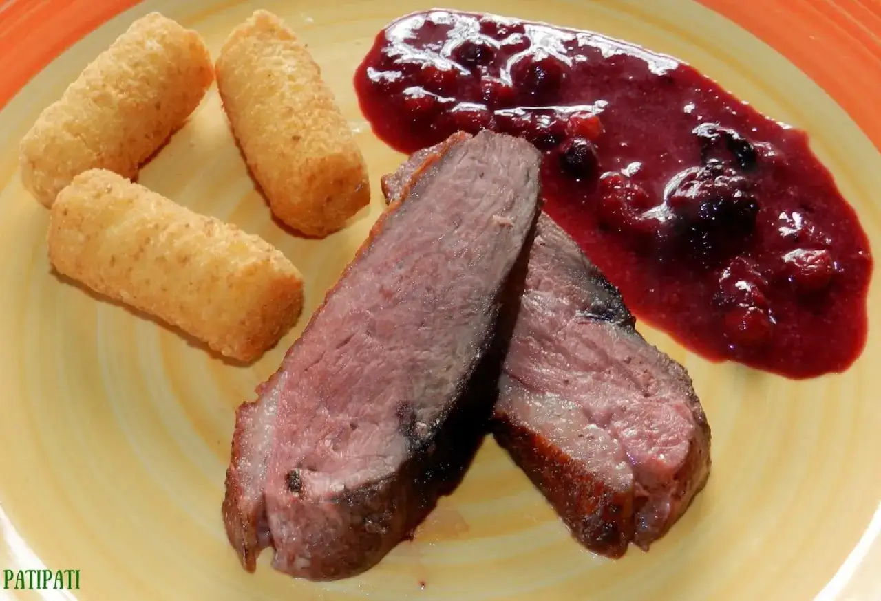 Magret de canard tranché, accompagné de croquettes dorées et d'une sauce aux fruits rouges, parfaite pour sublimer ce plat.