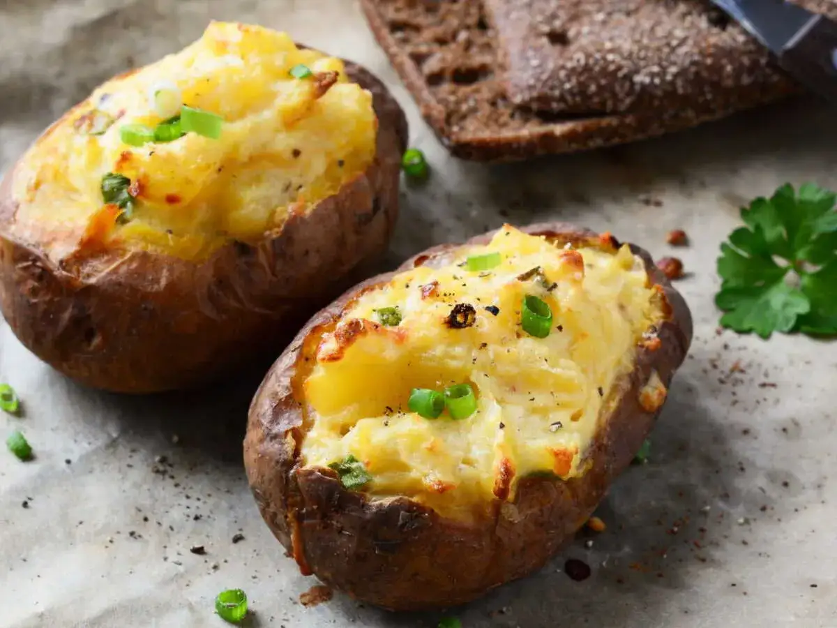 Deux pommes de terre farcies dorées, garnies de ciboule fraîche, prêtes à être dégustées avec une tranche de pain noir.