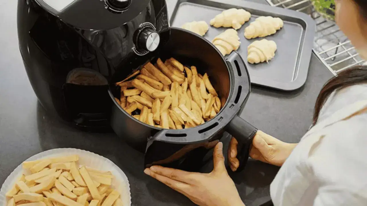 Une personne prépare des frites dans un air fryer. Des croissants crus attendent sur une plaque.