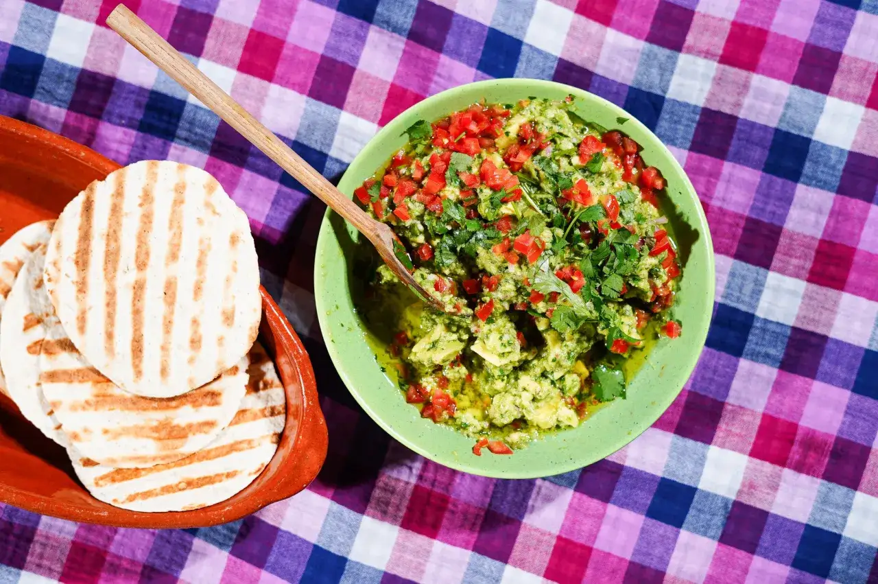 Un bol de recette guacamole traditionnel, garni de d&eacute;s de tomates et de coriandre fra&icirc;che, &agrave; c&ocirc;t&eacute; de tortillas grill&eacute;es dans un plat en terre cuite.