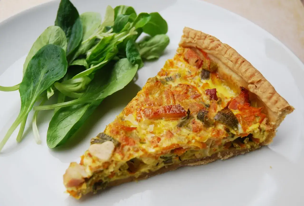 Une part de quiche aux l&eacute;gumes, garnie de carottes et poireaux, accompagn&eacute;e d'une salade verte fra&icirc;che.