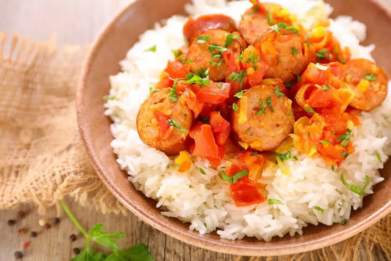 Un plat de rougail saucisse savoureux, avec des morceaux de saucisses et de tomates sur un lit de riz blanc, garni de persil frais.