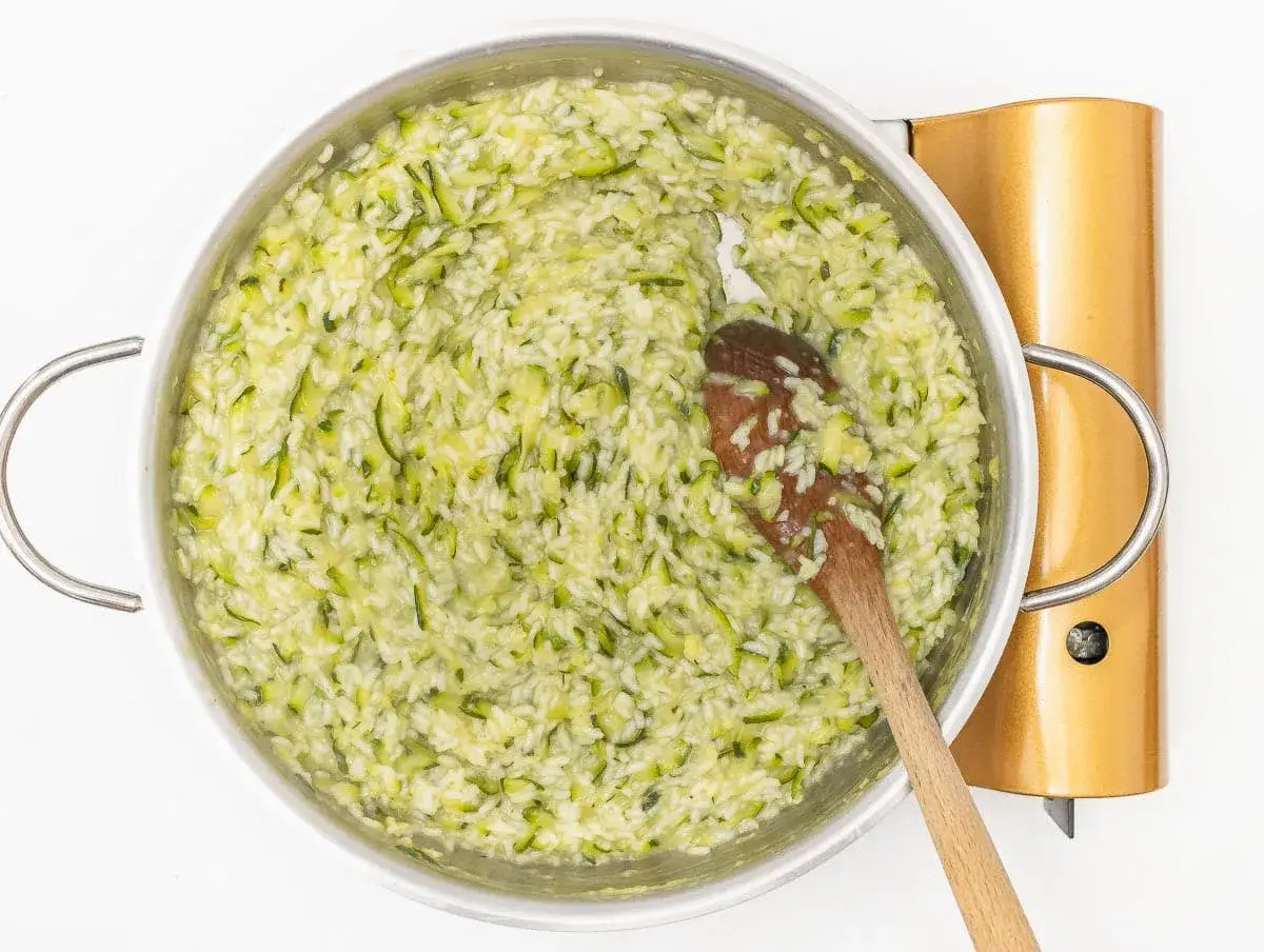 Risotto courgette cookeo cr&eacute;meux, pr&ecirc;t &agrave; &ecirc;tre d&eacute;gust&eacute;. Une cuill&egrave;re en bois remue ce plat savoureux.