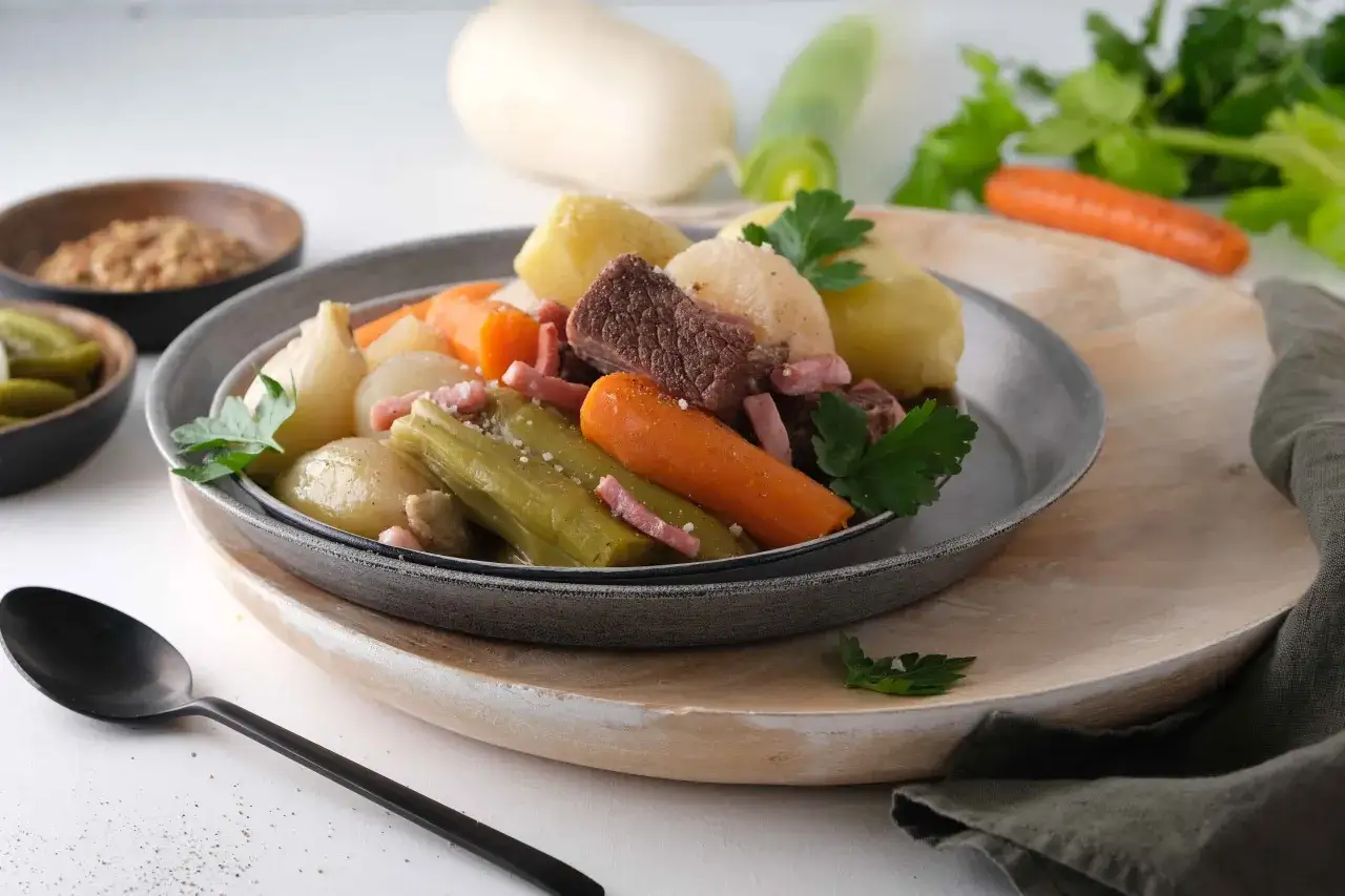 Un plat de pot-au-feu Cookeo, avec viande, carottes, poireaux et pommes de terre, servi avec des cornichons et de la moutarde.