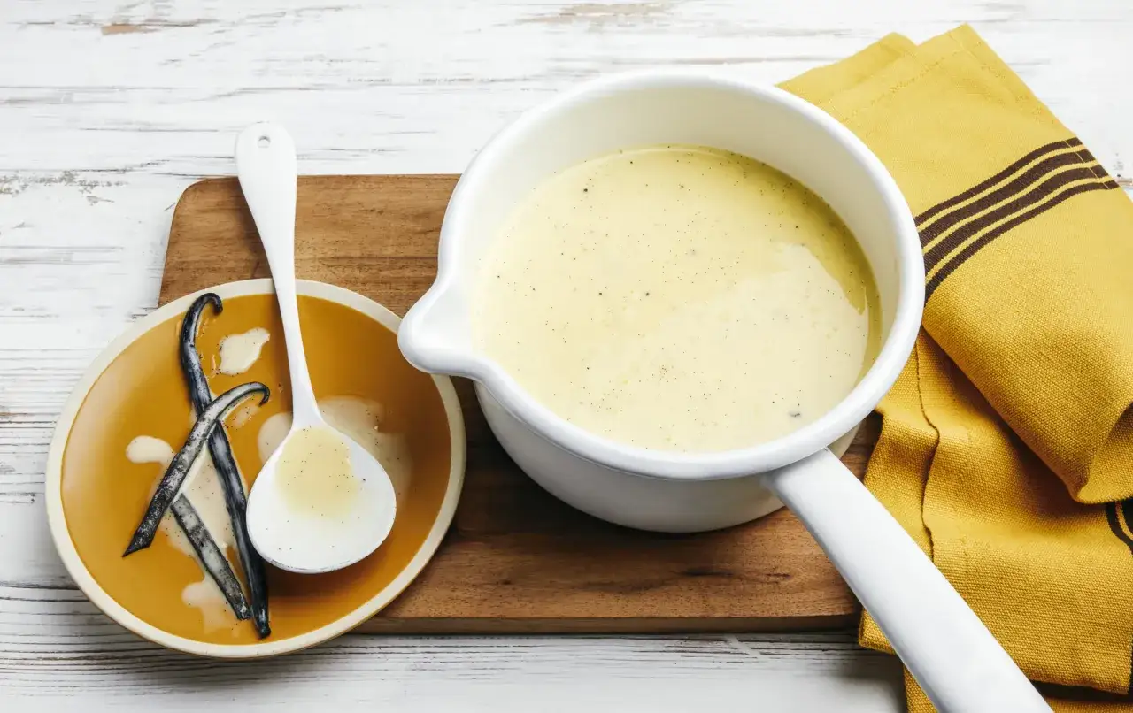 Une casserole de cr&egrave;me anglaise onctueuse, avec des gousses de vanille sur une assiette.