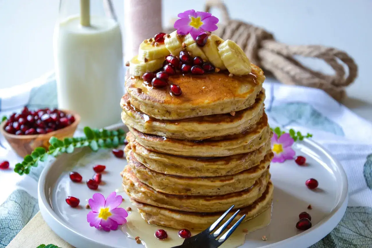 Pile de pancakes banane sans oeuf, garnis de rondelles de banane, de graines de grenade et de quelques &eacute;clats de noix. Un d&eacute;lice visuel et gustatif.
