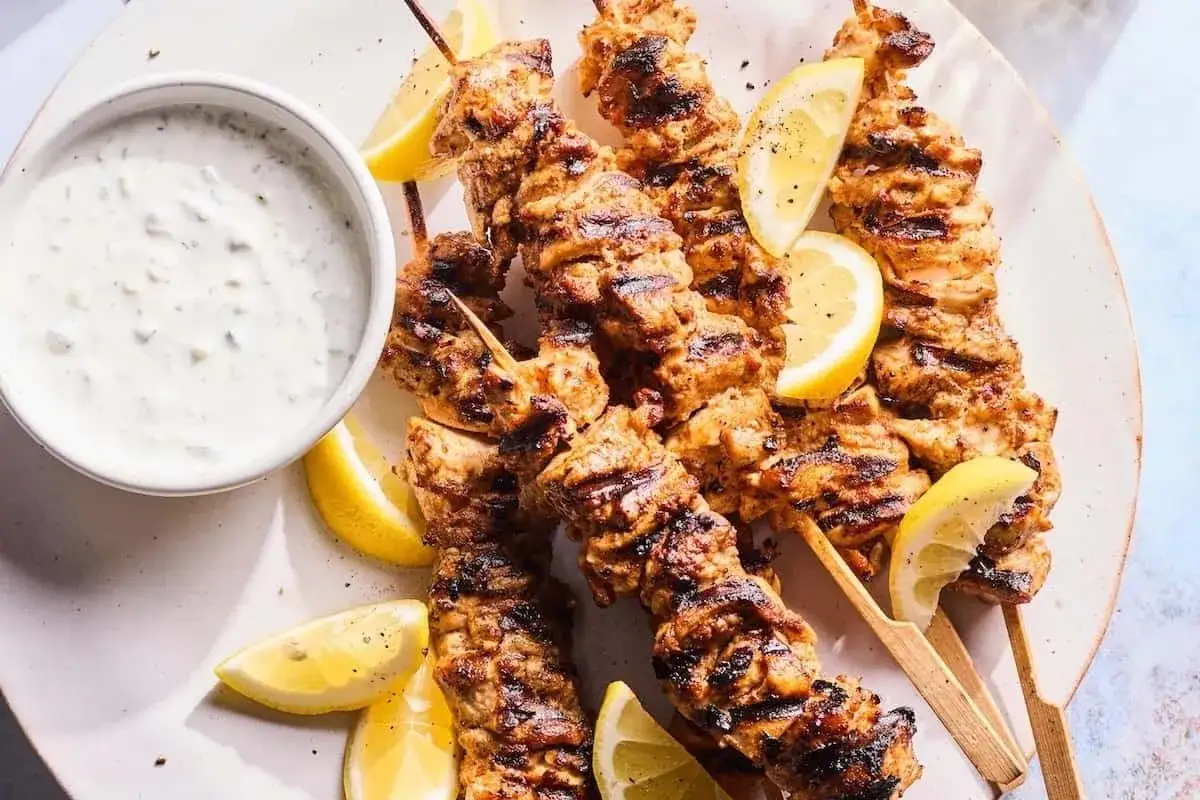 Brochettes de poulet grillé, savoureuses et juteuses, prêtes à être dégustées avec une sauce crémeuse et des quartiers de citron. La marinade brochette poulet a fait son œuvre !