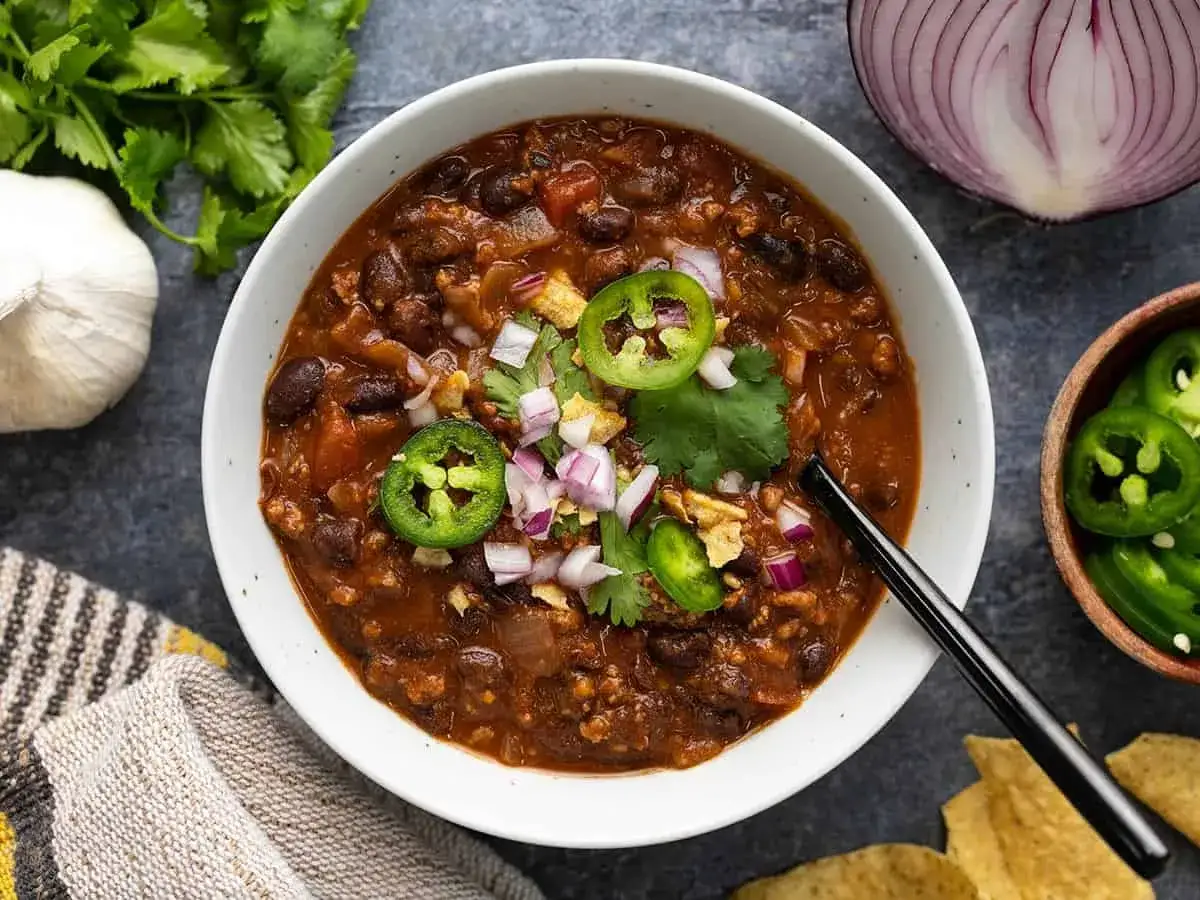 Un bol de chili con carne fumant, garni de jalapeños, oignons rouges et coriandre. Parfait pour un repas réconfortant.