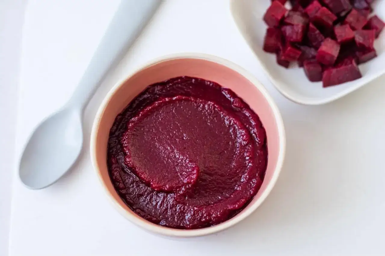 Un bol de pur&eacute;e de betterave onctueuse, avec des d&eacute;s de betterave coup&eacute;s en arri&egrave;re-plan. Une cuill&egrave;re est pos&eacute;e &agrave; c&ocirc;t&eacute;.