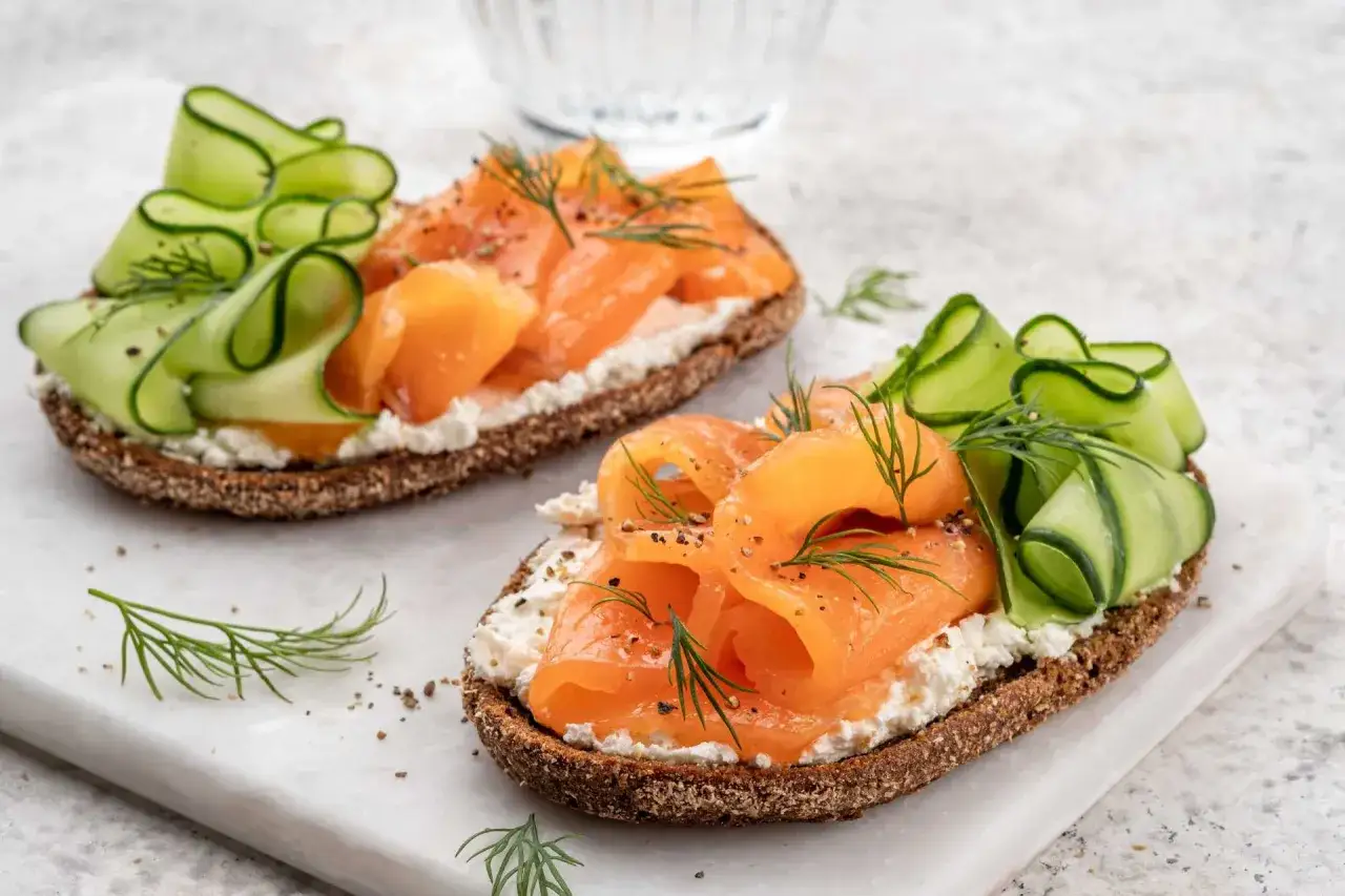 Deux tartines de rillettes de saumon, fromage frais, concombre en rubans et aneth, sur pain de seigle.
