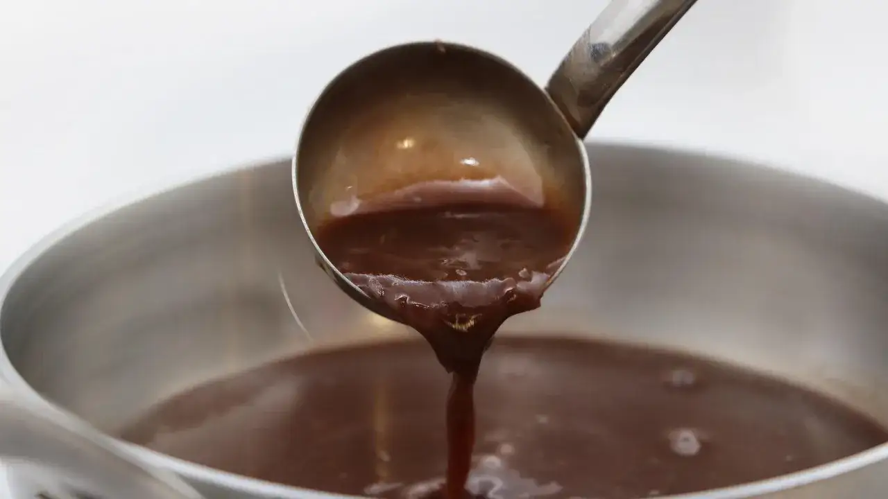 Une louche verse une sauce marchand de vin onctueuse dans une casserole.