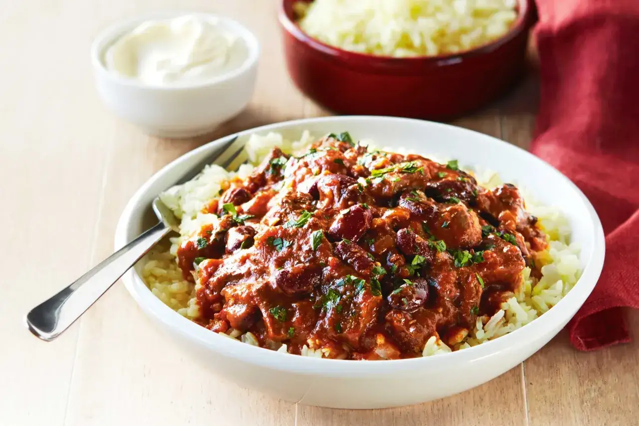 Un plat réconfortant de chili con carne et riz, garni de persil frais. Une touche de crème aigre est servie à côté.