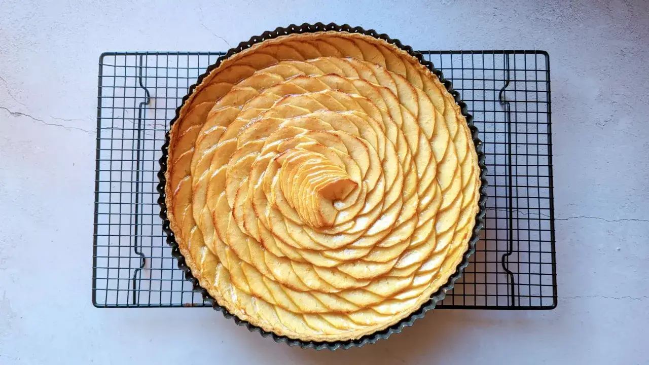 Tarte aux pommes magnifiquement d&eacute;cor&eacute;e de fines tranches de pommes dispos&eacute;es en spirale sur une grille de refroidissement.