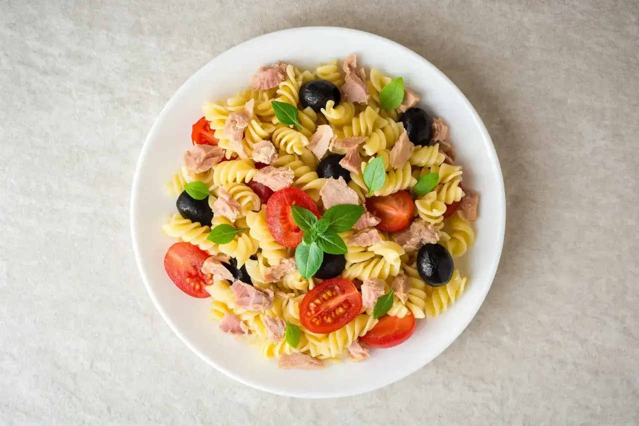 Une délicieuse salade de pâtes fusilli garnie de thon, tomates cerises, olives noires et basilic frais.