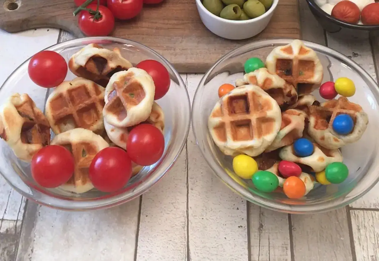 Deux bols de mini gaufres, l'un avec des tomates cerises, l'autre avec des bonbons colorés. La pâte à gaufre est prête à être dégustée !