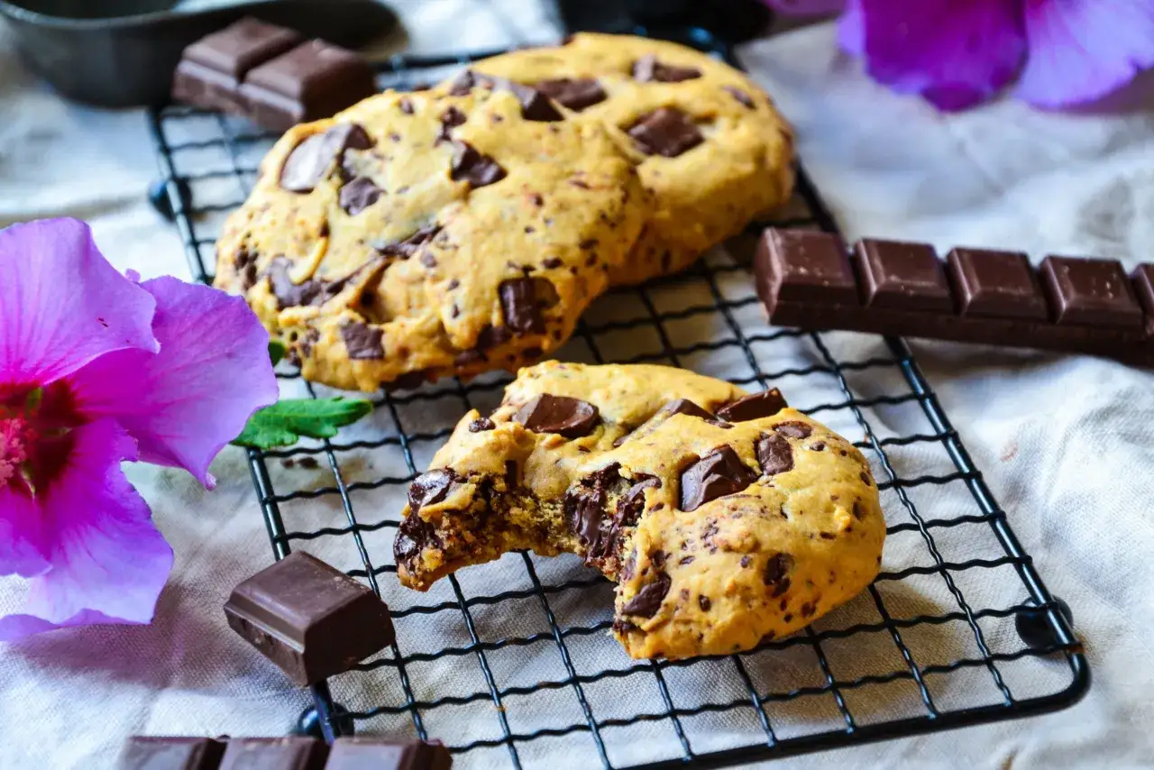 Délicieux cookies aux pépites de chocolat, parfaits pour une recette facile. Du chocolat noir et une fleur rose complètent la scène.
