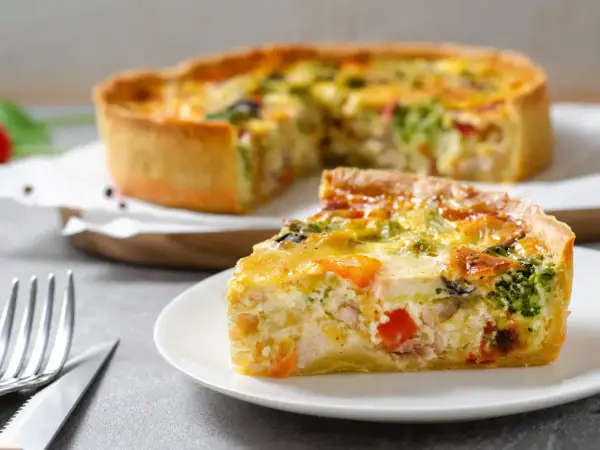 Une part de quiche savoureuse, garnie de poulet, brocolis et poivrons, repose sur une assiette. La pâte à quiche dorée est parfaite.